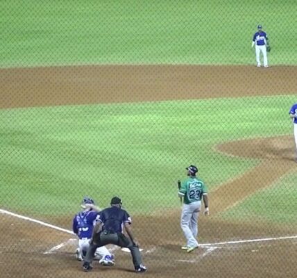 A baseball game in progress with the pitcher preparing to throw to a batter in a green jersey