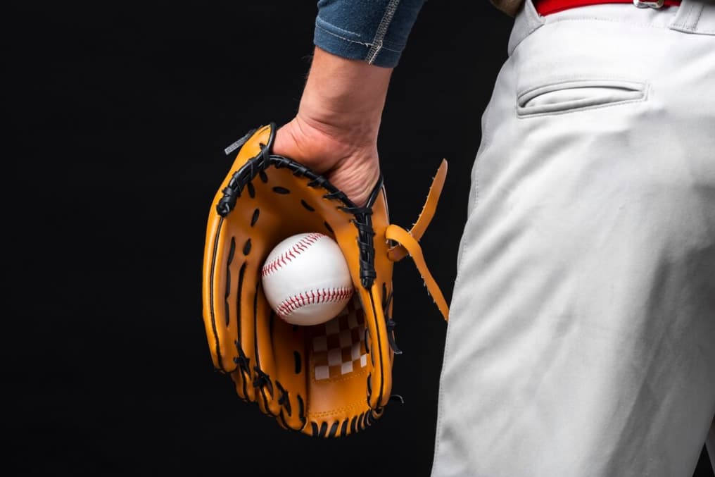 Person holding a baseball glove with a ball against a black backdrop